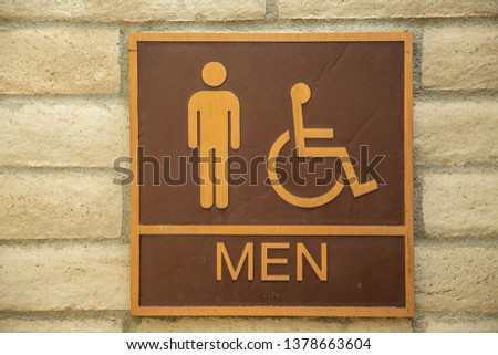 Mens restroom sign with handicap symbol on an adobe brick wall