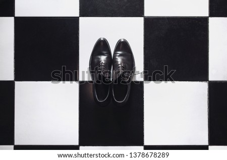 Black leather shoes stand on the floor against the background of a square black and white tile. Stylish shoes for sale and holiday.