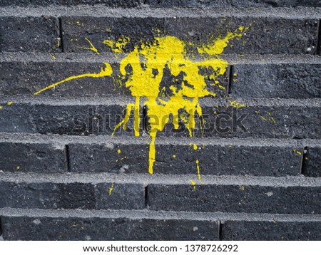 Fresh spot of bright yellow paint on old gray brick wall as a mark, symbol or graffiti. Abstract background with picturesque color blot in close-up street photo.