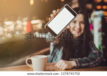 blurry portrait of a happy smiling brunette girl who holds a mobile phone with a clean screen ready for your logo or text

