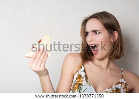Screaming brunette woman student eating a sandwich over a grey background. Space for text