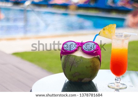 Coconut with sunglasses on a swimming pool background.