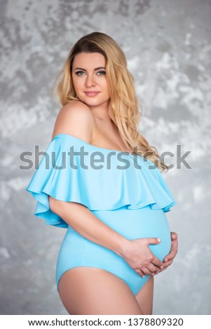 Beautiful young pregnant blonde woman in a blue suit body against a gray concrete wall background. Women's health and beautiful pregnancy