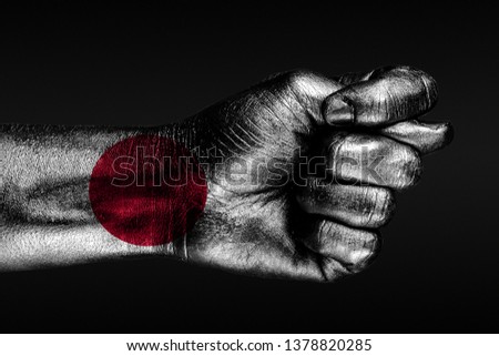 A hand with a painted Japan flag shows a fig, a sign of aggression, disagreement, a dispute on a dark background. Horizontal frame