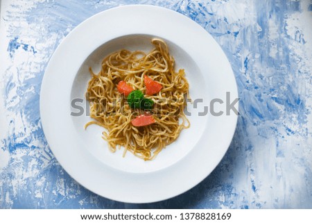 
Italian spaghetti with salmon and spinach on a white plate. Delicious dinner, rich food. Painted blue background.