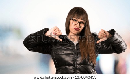 Woman with glasses showing thumb down at outdoors