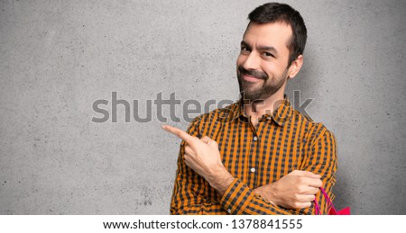 Man with shopping bags pointing to the side to present a product over textured wall
