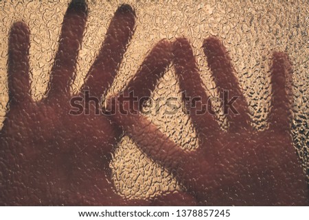 Hands of the victim, asking for help behind a blurred glass. Spooky background