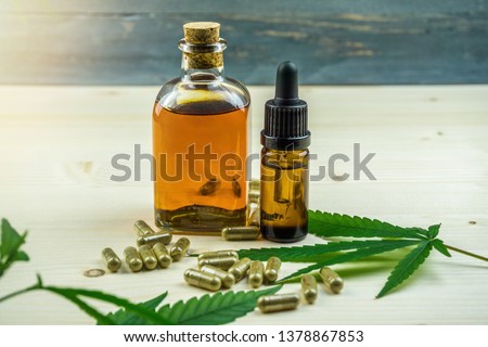 Clear CBD Cannabidiol capsules and cannabis oil on wooden backdrop Royalty-Free Stock Photo #1378867853