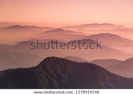 View of Himalayas mountain range with visible silhouettes through the colorful fog from Khalia top trek trail. Khalia top is at an altitude of 3500m himalayan region of Kumaon, Uttarakhand, India. Royalty-Free Stock Photo #1378914548