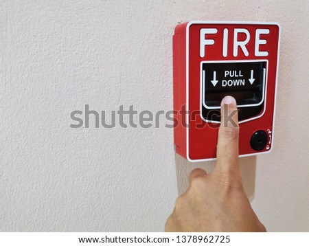 Hand pulling down fire alarm. Manual fire alarm system. T-bar fire alarm pull station on grey concrete wall background.