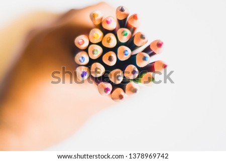Top view of a bunch of colored pencils held together by a hand on white background with shallow depth of field