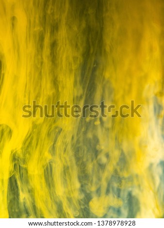 Yellow paint dissolving into water, close up view. Blurred background. Acrylic ink flows mixing with liquid, abstract pattern. Droplet of ink transformation in water, abstract background.