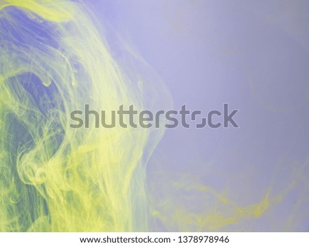 Yellow and lilac acrylic paint in water, close up view. Blurred background. Acrylic light clouds dissolving into water, abstract background. Ink mixing with liquid, abstract pattern