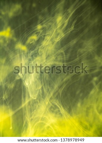 Yellow paint dissolving into liquid, close up view. Blurred background. Acrylic smoke swirling under water, abstract pattern. Paint clouds mixing with water, abstract background. Abstract art