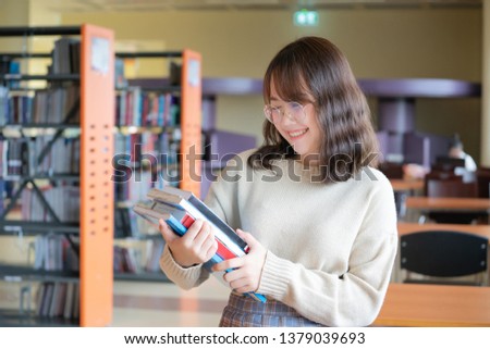 Happy Asian woman looking for a book in a library. Woman reading book in an university library. Library and Education concept.