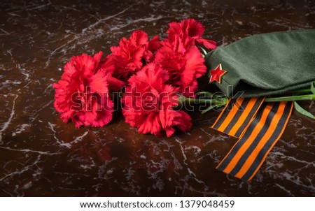 on the background of the monument, a bouquet of red carnations, military cap and St. George ribbon, close-up
