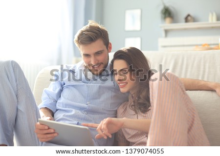 Young couple in pajamas watching media content online in a tablet sitting on the floor in the living room. Royalty-Free Stock Photo #1379074055