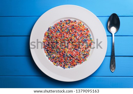 White plate with color preparations (vitamins, dyes, flavor enhancers, nutritional supplements, innovative technologies, candy sweets) on an blue wooden table background.