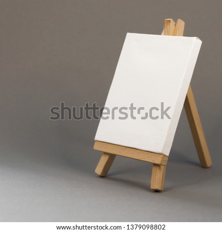 Blank white canvas on easel on gray background