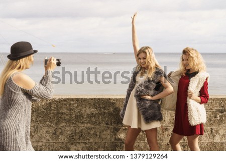 Three females friends having fun during outdoor photo session. Woman taking pictures of two during warm autumn weather.