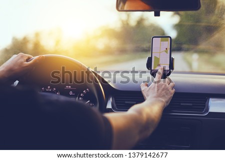 Driver using GPS navigation in mobile phone while driving car at sunset Royalty-Free Stock Photo #1379142677