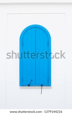 One small arched blue door with metal hinges on a plain white wall