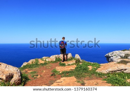 Adult traveler stands on the edge of cliff and takes some picture. Younger, blue sky, blue sea. Human is on the top of hill and enjoying view to down on mediterranean sea in Cyprus nearby Poli city.