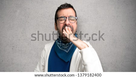 Handsome man with glasses yawning and covering wide open mouth with hand over textured wall