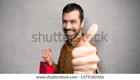 Man with shopping bags giving a thumbs up gesture because something good has happened over textured wall
