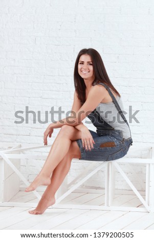 Young female in jeans overalls sitting