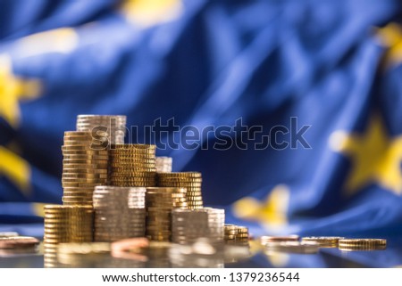 Towers with euro coins and flag of European Union in the background.  Royalty-Free Stock Photo #1379236544