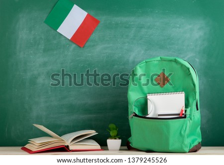 Learning languages concept - green backpack, flag of the Italy, books and notebooks on the background of the blackboard Royalty-Free Stock Photo #1379245526
