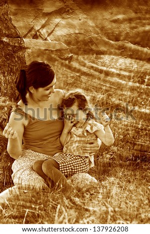 retro sepia photo, mother, daughter, woman and child sitting grass near tree family photo on their faces joy and emotion