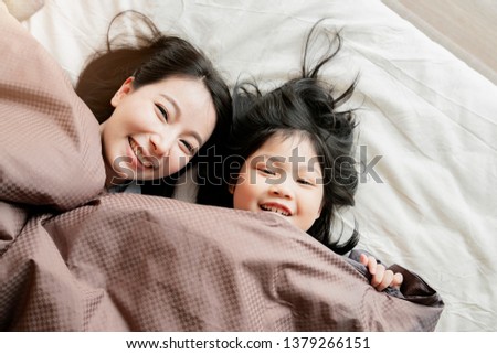 happiness asian family moment mom and daughter play and laydown with blanket on white bed home interior background