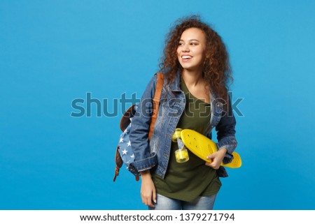 Young african american girl teen student in denim clothes, backpack hold skate isolated on blue background studio portrait. Education in high school university college concept. Mock up copy space