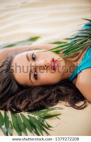 beautiful girl posing with green leaves and Looking At Camera while lying on beach