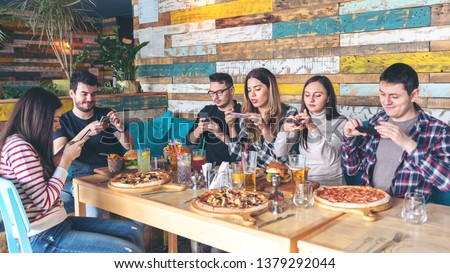 Social media addiction concept with young people photographing food in rustic restaurant – happy friends taking picture of pizza and hamburgers with mobile phones to post online, connected millennials