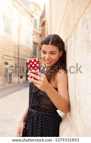 Beautiful young tourist woman visiting city street sightseeing, holding smartphone taking selfies photos, networking outdoors. Female using technology, fun travel leisure recreation lifestyle.