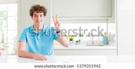 Wide shot of young handsome man at home showing and pointing up with fingers number two while smiling confident and happy.