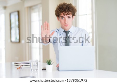 Young business man working with computer laptop at the office doing stop sing with palm of the hand. Warning expression with negative and serious gesture on the face.