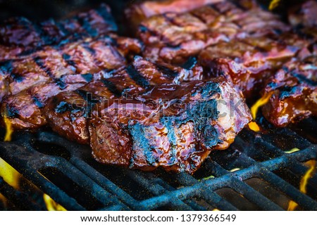 Boneless beef ribs grilling over flames with added barbecue sauce. Extreme shallow depth of field with blurred background with focus on front meat.