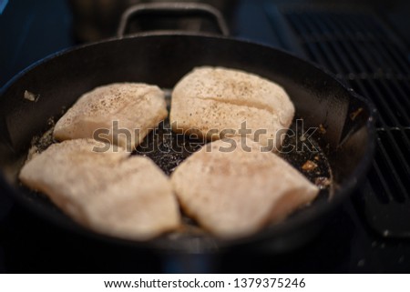 Cod fish being fried or cooked in a cast iron frying pan with melted butter on a stove.