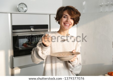 Smiling brunette woman having dinner and looking at the camera while standing at kitchen
