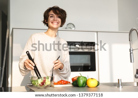 Picture of Happy brunette woman looking away while cooking by the table at kitchen