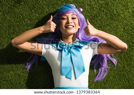 Smiling asian anime girl lying on grass and showing thumbs up