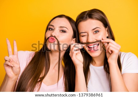 Close up photo two people beautiful she her ladies models send air kisses playing make fake moustache crazy winking eye show v-sign wear white pink casual t-shirts isolated yellow background