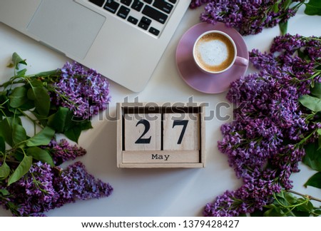 Wooden cubes calendar May 27. Home office desk in lilac colors with, cup of coffee, laptop, lilac flowers on a white background. Flat lay Business womans workplace. Top view. Copy space
