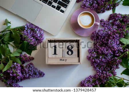 Wooden cubes calendar May 18. Home office desk in lilac colors with, cup of coffee, laptop, lilac flowers on a white background. Flat lay Business womans workplace. Top view. Copy space