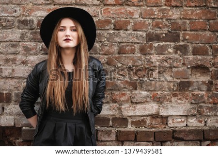 Young beautiful girl in a hat and with a dark make-up outside. Girl in the Gothic style on the street. A girl walks down the city street in a leather waistcoat with phone.
